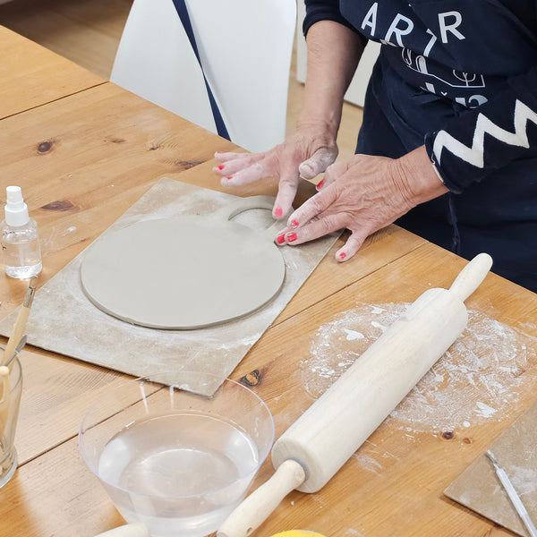 Person working with clay on a wooden table with various tools