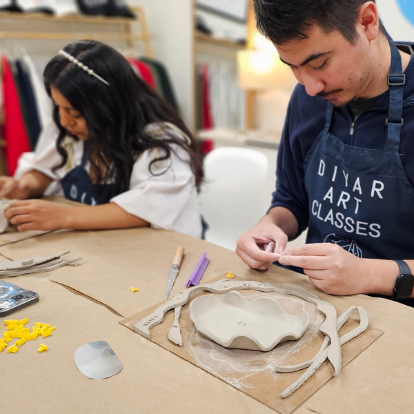 Two people working on pottery in a classroom setting