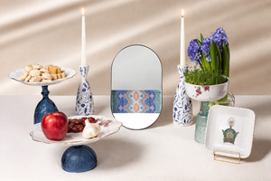 Decorative items including a mirror with a colorful pattern, candles, a vase with flowers, and a fruit platter on a table. Haftsin Haftseen Nowrouz Persian new year