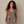 A woman modeling a taupe two-piece linen set consisting of a sleeveless cropped vest with buttons and matching wide-leg harem pants, standing against a neutral beige wall.