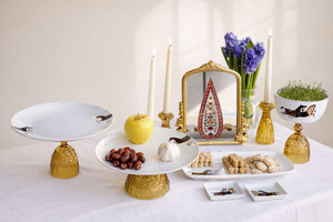 Decorative table setting with gold stands, fruits, candles, and a small mirror. haftsin haftseen Persian new year nowruz norooz