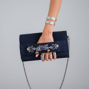Person wearing a white lace top and blue jeans, holding a black clutch with decorative elements.
