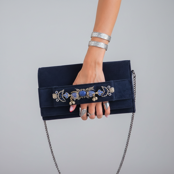 Person wearing a white lace top and blue jeans, holding a black clutch with decorative elements.