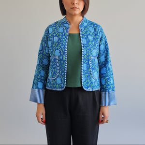 Person in blue patterned jacket standing by a teal door.