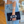 Person holding a black clutch with floral design, wearing lace sleeves and denim jeans.