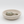 A round, shallow stone vessel sink or incense holder in a light beige speckled texture, featuring a small gold metal  holder in the center, set against a seamless light gray background.