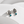 A pair of silver-toned drop earrings with an openwork leaf design and a small round turquoise blue stone at the bottom, displayed on a white curved surface.