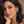 A woman with dark wavy hair poses in a close-up portrait, wearing a delicate silver bracelet with a round turquoise cabochon and a matching silver drop earring with a floral filigree design and a small turquoise accent.
