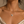 A close-up of a woman wearing a delicate silver Iran map necklace with a small evil eye pendant, styled with a cream satin camisole against a warm beige background.